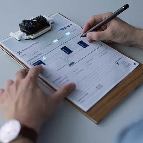 The photo shows IllumiPaper with an Industry 4.0 maintenance application. More specifically, a user can be seen touching and writing on an IllumiPaper sheet, with certain areas illuminated in blue.